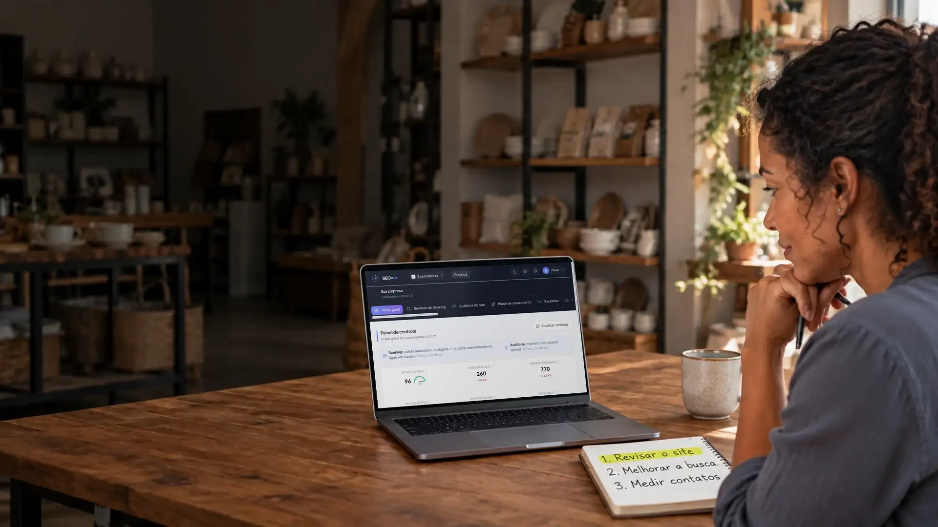 Empresária na própria loja acompanhando uma análise do site no notebook, com três prioridades anotadas no caderno