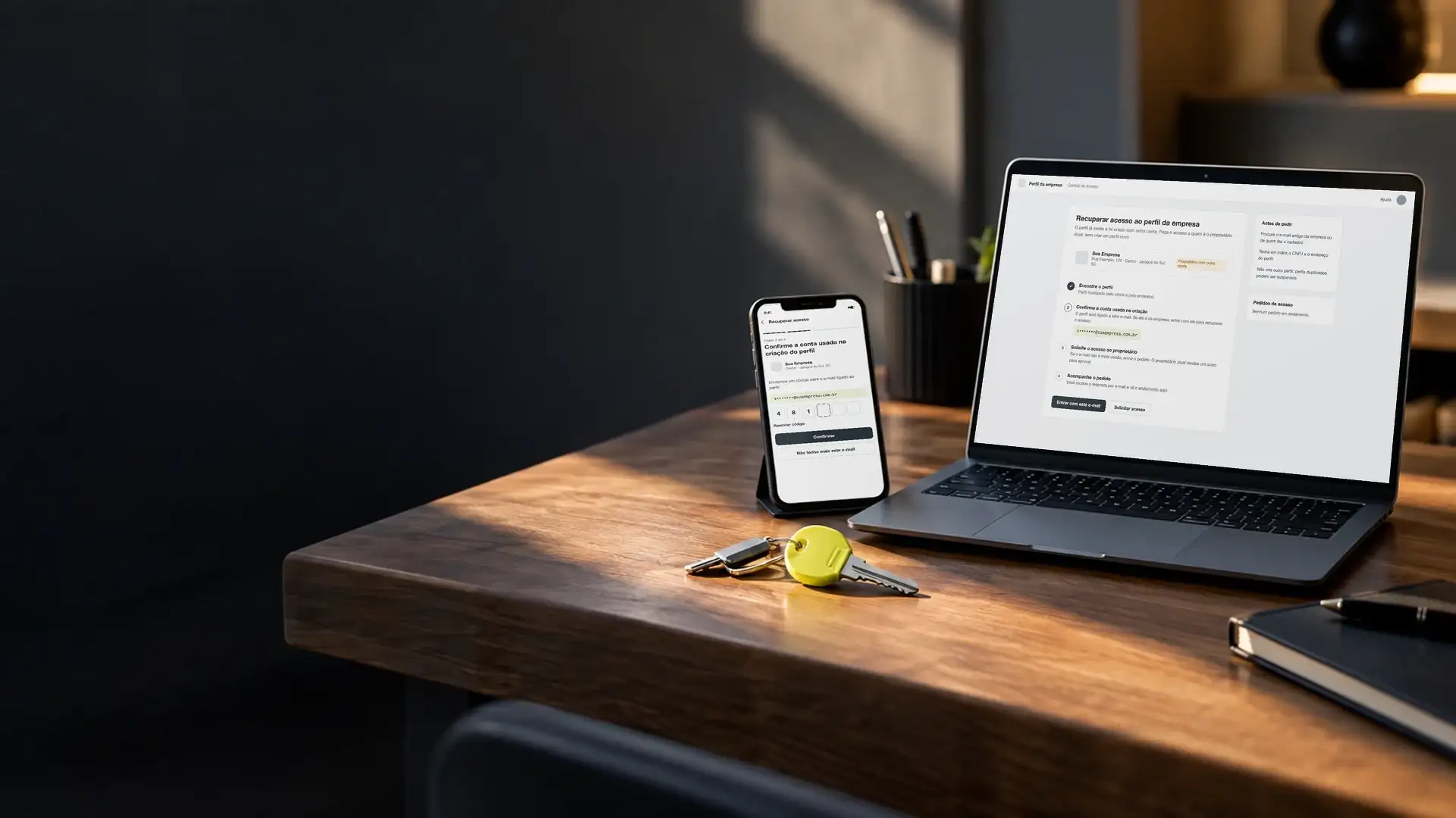 Celular e notebook com a tela de recuperação de acesso ao perfil da empresa, e um molho de chaves na mesa