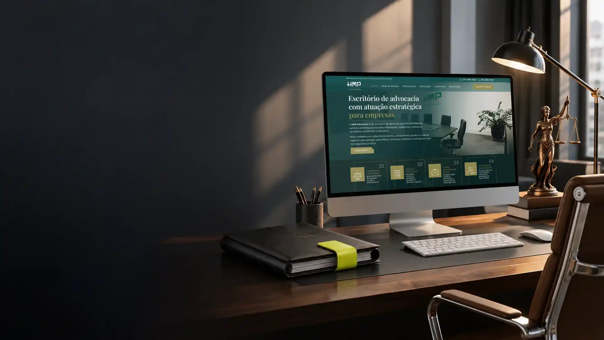 Monitor com o site de um escritório de advocacia, ao lado de uma estátua da justiça e de uma luminária
