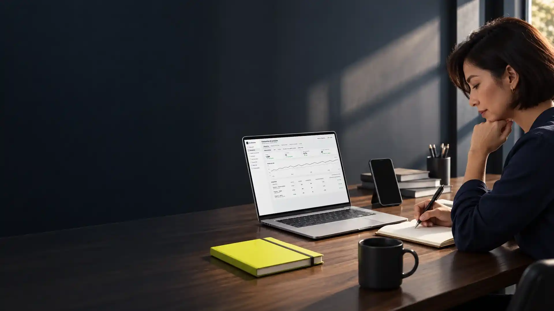 Mulher analisando no notebook o painel de campanhas de anúncios no Google, com um caderno aberto ao lado